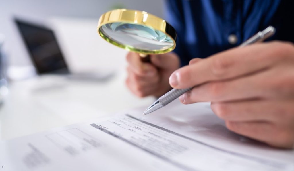 Professional examining documents with a magnifying glass during a root cause investigation to verify evidence and identify contributing factors.