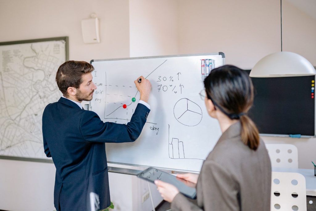 Project manager presenting performance metrics and workflow changes on a whiteboard during a Change Control Board review meeting.