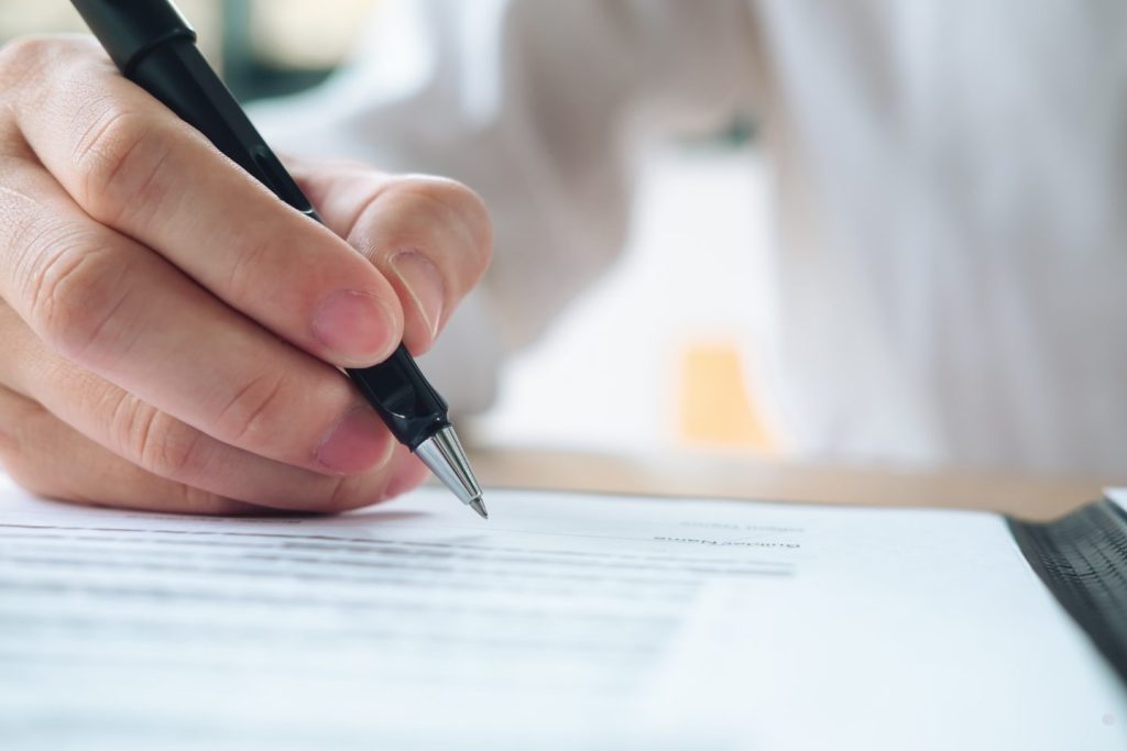Close-up of a person signing a document with a pen for a letters of recommendation sample topic.
