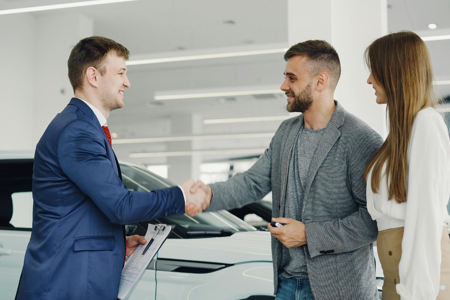 Sales representative shaking hands with customers in a car showroom after completing a successful vehicle purchase agreement.