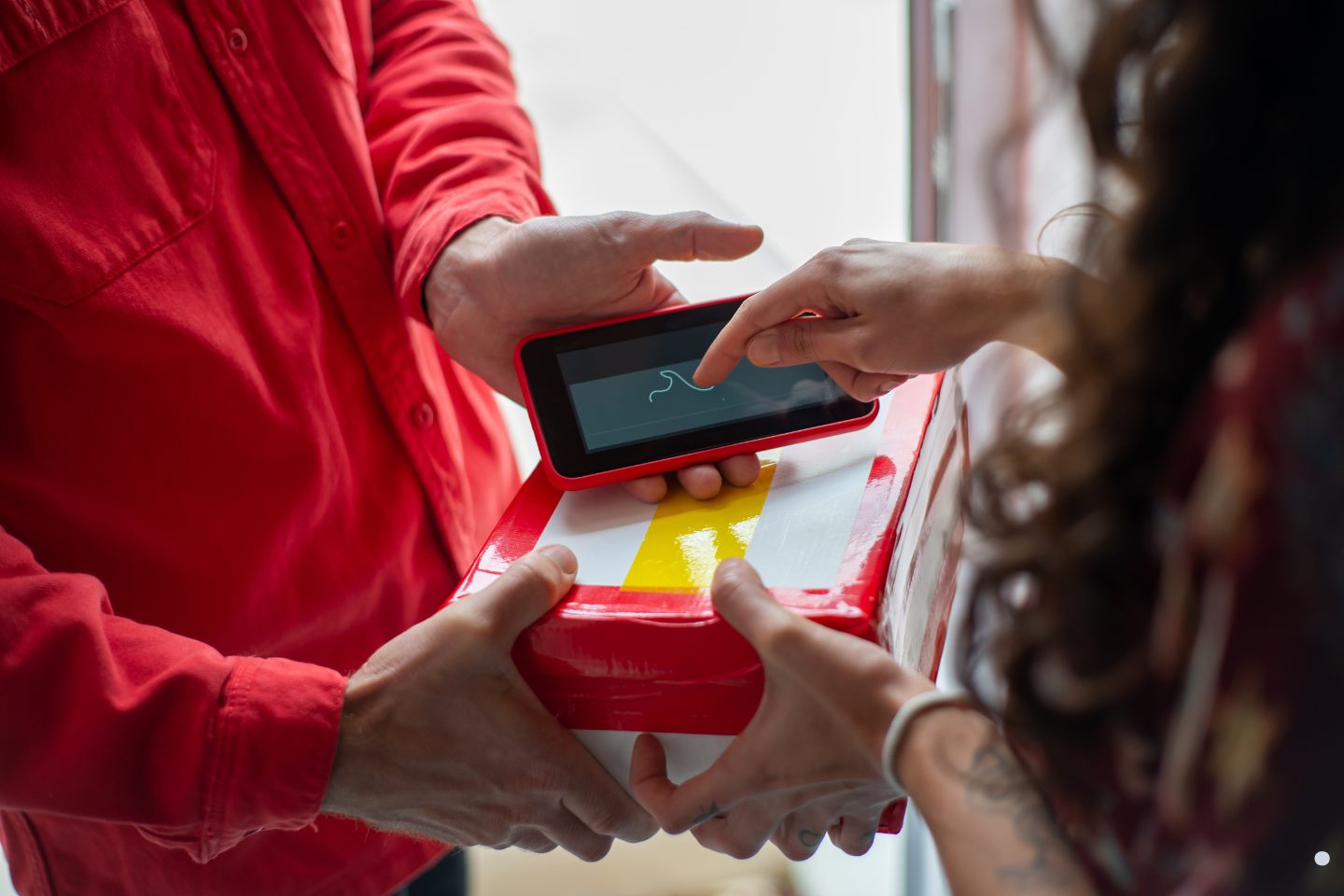 Customer signing digitally on a handheld device while receiving a package delivery from a courier service.