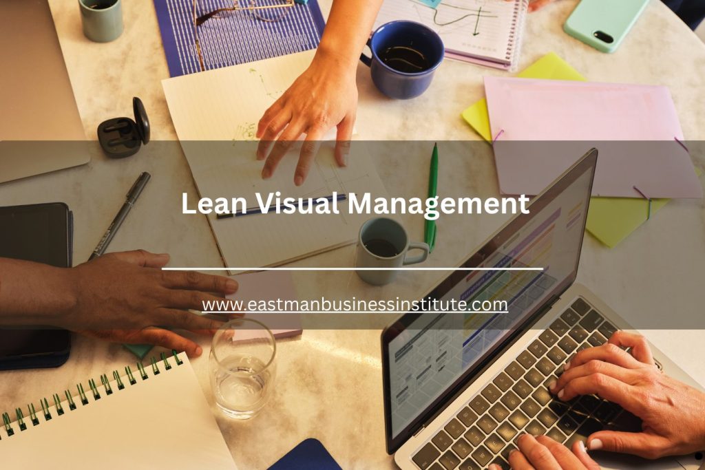 Top view of a collaborative office workspace with laptops, notebooks, and planning materials focused on lean visual management strategies.
