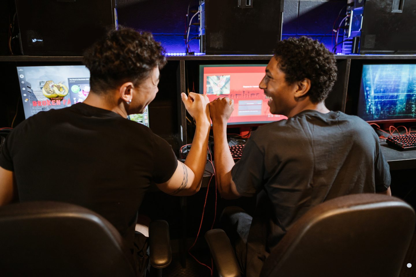 Two gamers celebrating a successful match while playing multiplayer video games at a computer gaming station.