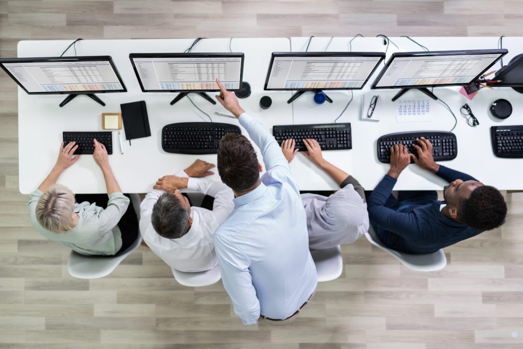 Top view of professionals working at computers analyzing data across multiple monitors
