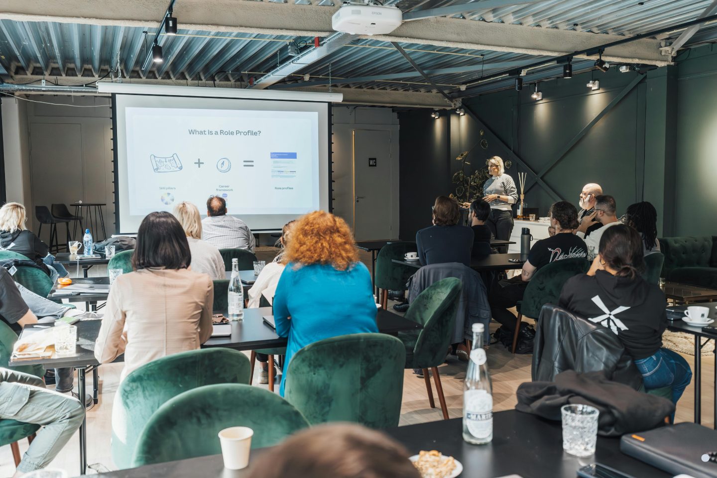 Group of professionals attending a business presentation with charts and process diagrams displayed on a screen.