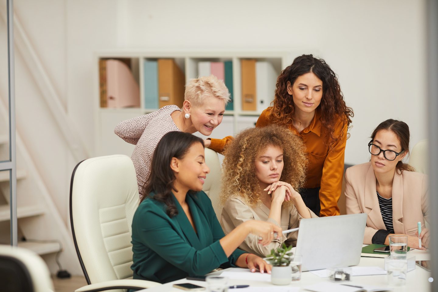 Team of professionals collaborating around a laptop while reviewing work and discussing ideas in a modern office setting