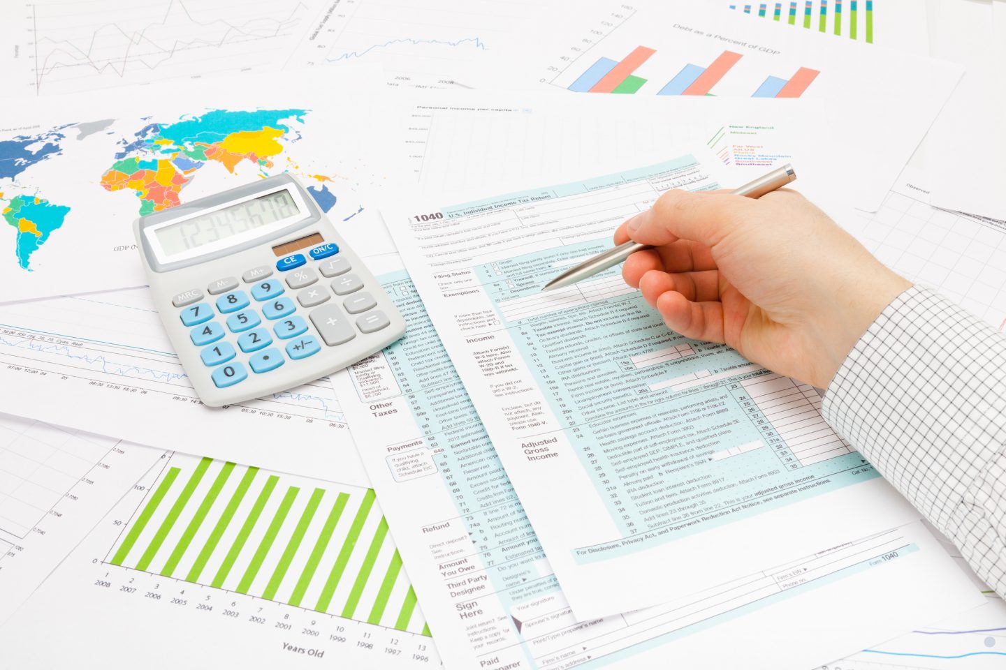 Person reviewing financial reports, tax documents, and charts with a calculator and pen for business analysis.